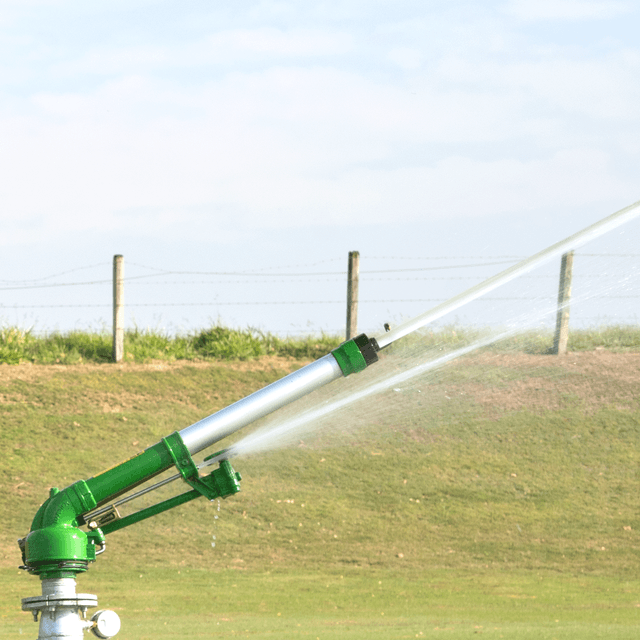 um campo de plantação bem verde com um trator a sua frente e aspersores jorrando água ao fundo