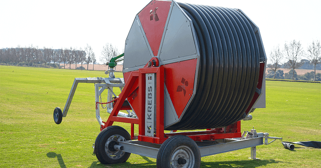 um pequeno campo de plantação a frente com um carretel com vários cabos enrolados nele e ao fundo na montanha uma cidade brasileira antiga
